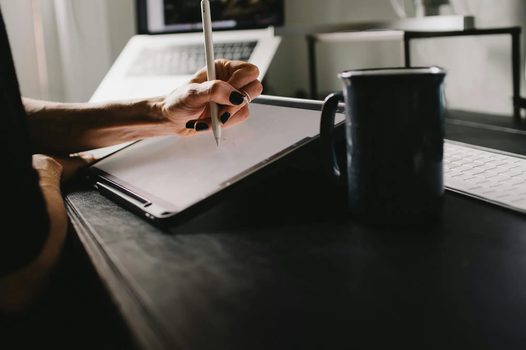 Hand holding a stylus over a tablet beside a coffee mug at the office
